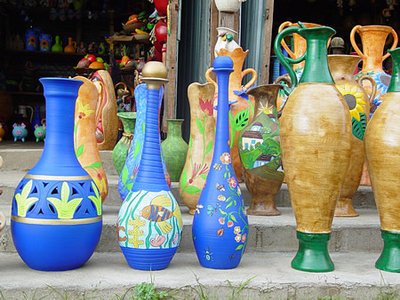 Jarrones, botellas y cántaros de cerámica pintada a mano en colores azul, verde y naranja exhibidos en escalones