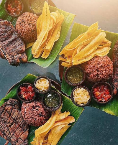 Comida nicaragüense servida sobre hoja de plátano: carne asada, arroz, plátano frito y soperos con salsas y encurtidos
