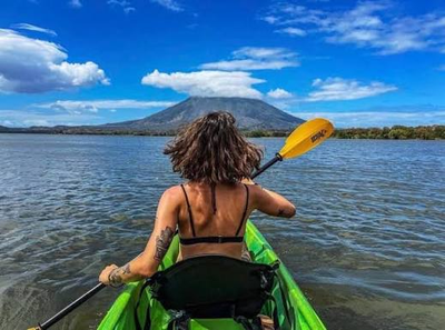 Kayakista remando hacia un volcán que emerge del lago bajo un cielo nublado