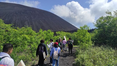 Grupo de caminantes en un sendero con un cono volcánico negro al fondo